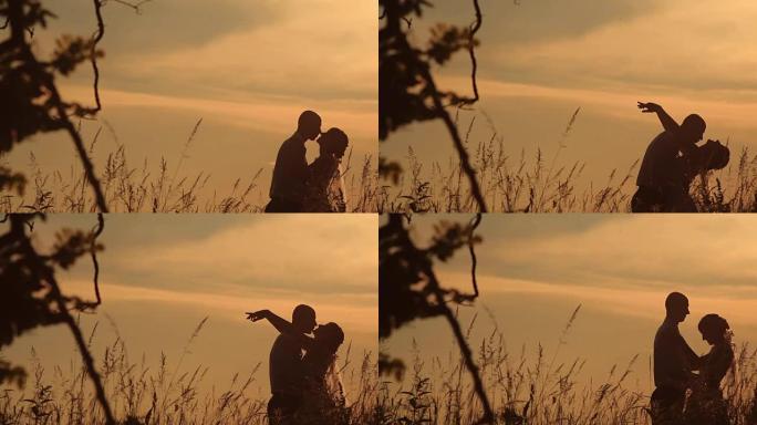 年轻夫妇在田野日落的背景上轻吻