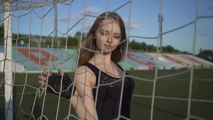 年轻女子运动员走到足球场，碰到了网门