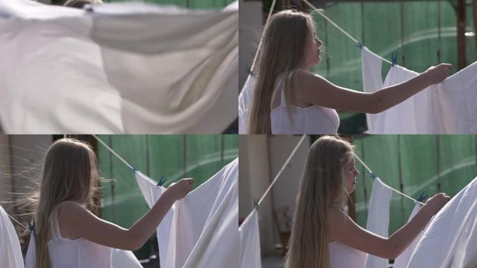年轻的金发女孩把湿衣服挂在晾衣绳上，在后院晾干