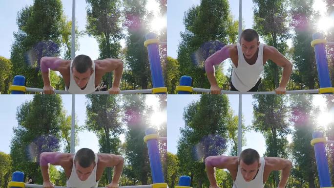 运动男子在城市公园运动场的酒吧做俯卧撑。强壮的年轻肌肉发达的家伙在夏天户外训练。运动员在操场上锻炼。