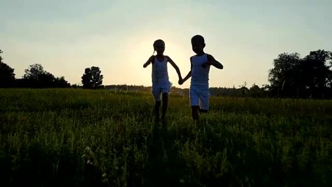 夏天日落时，在太阳的背景下，孩子们，男孩和女孩的身影正在奔跑，玩得开心。幸福的家庭。慢动作