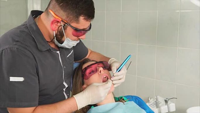 戴眼镜的正畸医生用激光使一名年轻女子的牙齿变白