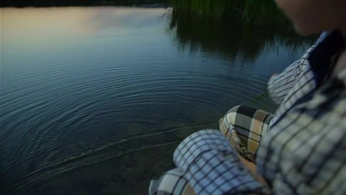 孤独的男孩在日落时在河水中与芦苇搏动