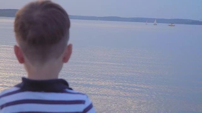 海滨穿着条纹背心的高加索男孩。在背景游艇上快乐，日落。