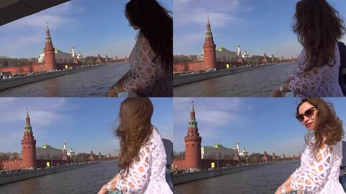 穿着白色连衣裙的年轻女子站在经过莫斯科克里姆林宫的船甲板上。去俄罗斯旅游概念。全高清镜头