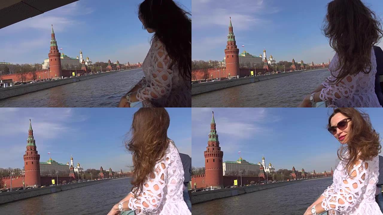 穿着白色连衣裙的年轻女子站在经过莫斯科克里姆林宫的船甲板上。去俄罗斯旅游概念。全高清镜头