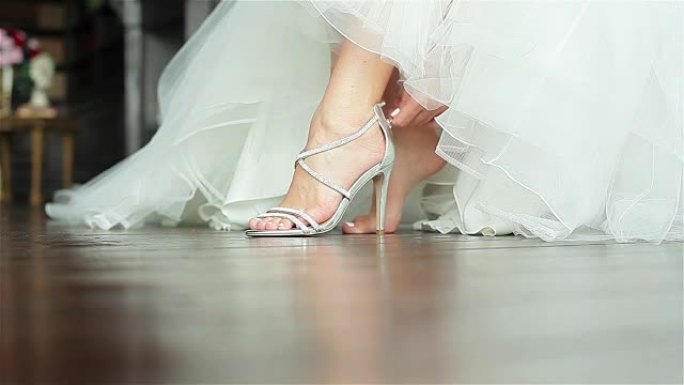 女人穿上鞋子手靠近浅层景深。新娘穿着华丽的白色礼服在豪华的高跟凉鞋上系上拉链，为婚礼上的舞蹈做准备
