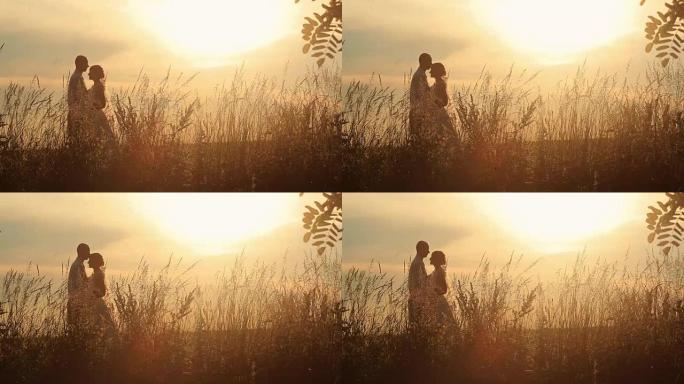年轻的已婚夫妇在田野日落的背景下轻吻