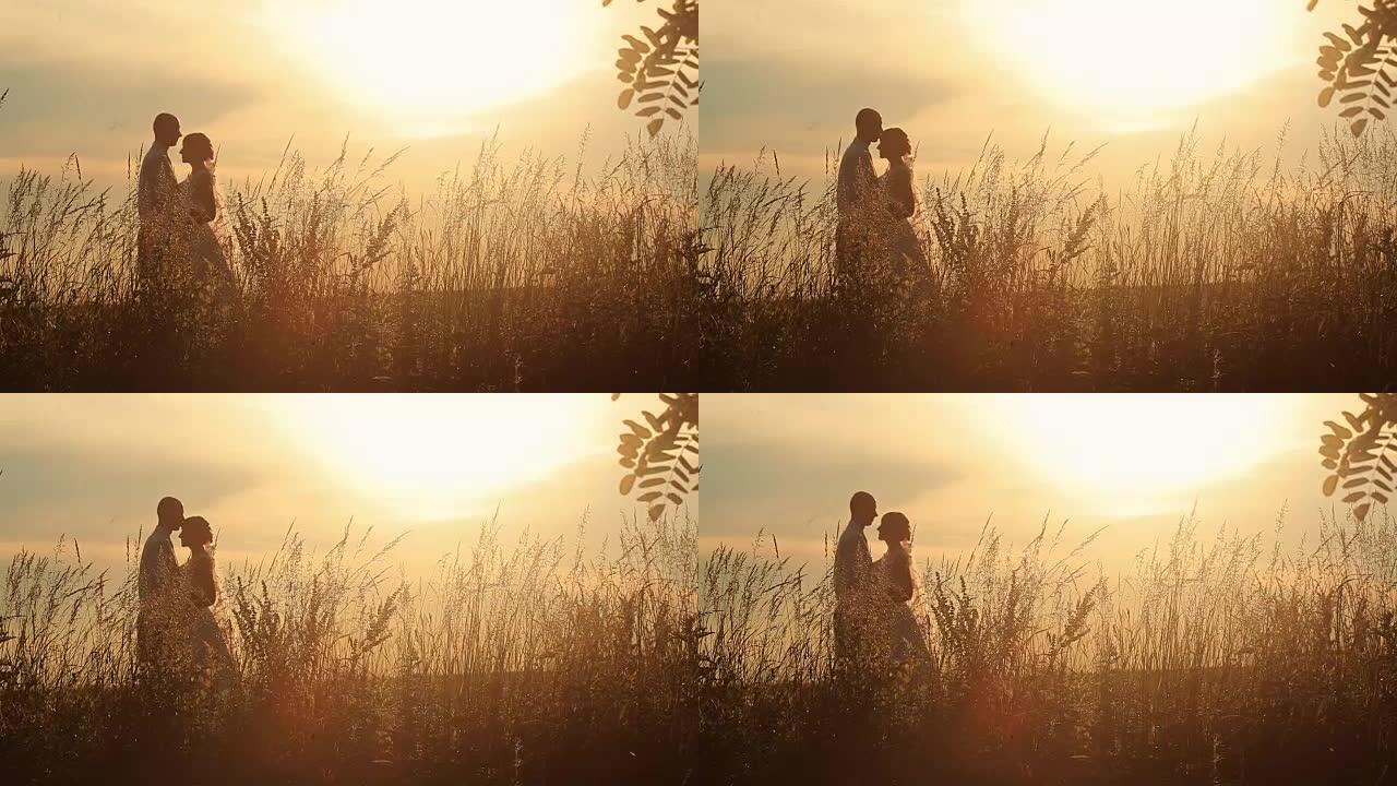 年轻的已婚夫妇在田野日落的背景下轻吻