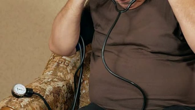 超重的人在沙发上测量自己家的压力。他通过血压计听脉搏