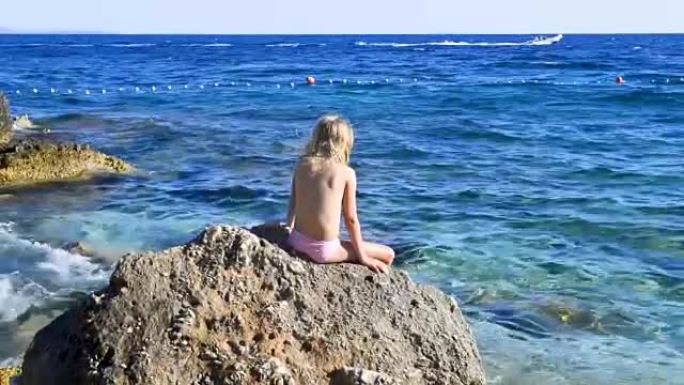 穿着泳衣坐在岩石上看着蓝色亚得里亚海的金发女孩的肖像