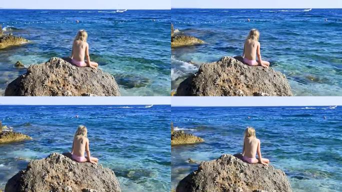 穿着泳衣坐在岩石上看着蓝色亚得里亚海的金发女孩的肖像