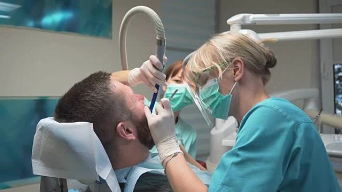 牙医在助手的帮助下钻男人的牙齿。稳定。