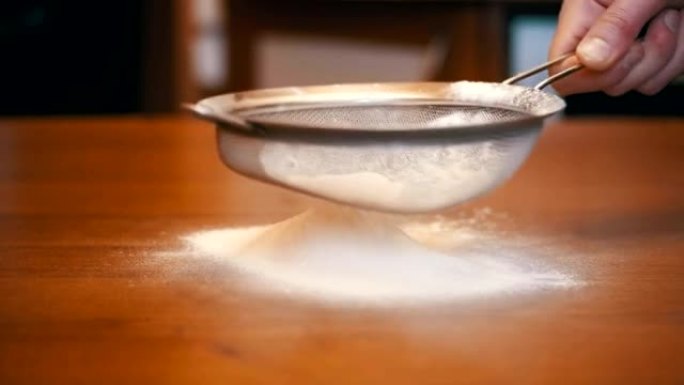 在家庭厨房的木桌上通过筛子筛分面粉。慢动作