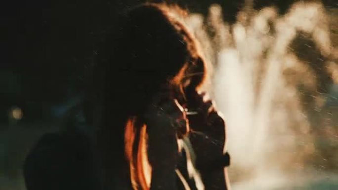 日落时在喷泉前的一个女孩的肖像。点，喷水喷泉。一个神秘的年轻女子。