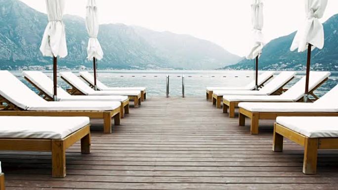 木制码头，带躺椅和太阳伞，在群山环绕的大海中 -- 避暑度假4k视频背景