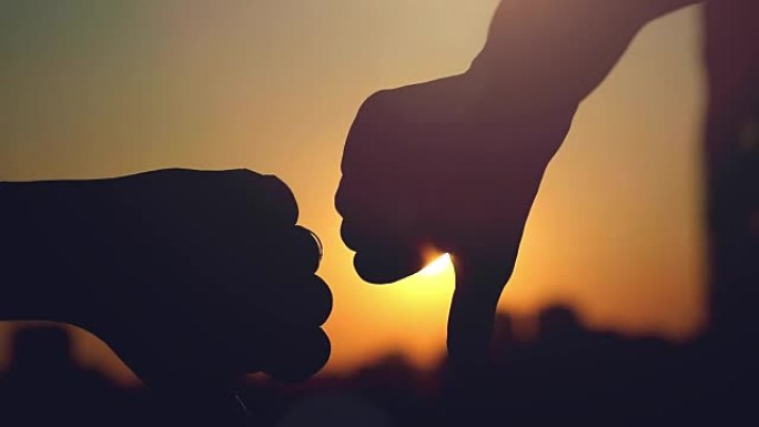 女性和男性手的慢动作在城市日落时通过太阳显示拇指向下的手势