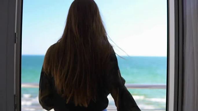 长发的女人打开阳台的门，眺望大海。享受外面的海景。慢动作镜头