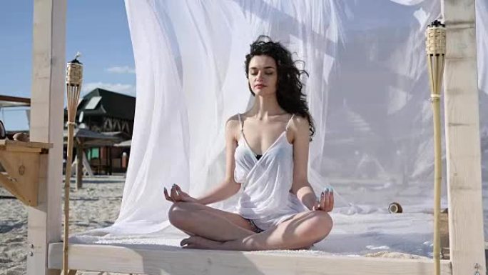 女性在平房上的莲花姿势冥想，夏天在海滩上瑜伽，风长出头发和白布，热带岛屿