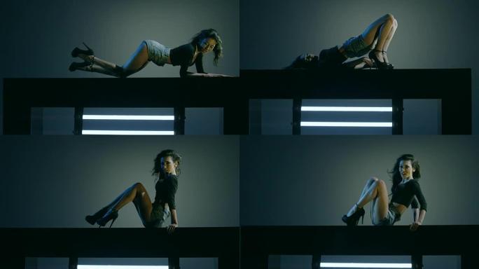 性感的黑发在蓝色深色背景上跳舞。美丽的女孩跳舞，躺在立方体上。在慢动作的红色史诗巨龙电影相机上拍摄。