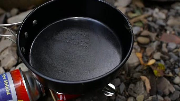 在河边的一个露营中，男人的手在露天的煎锅里倒油