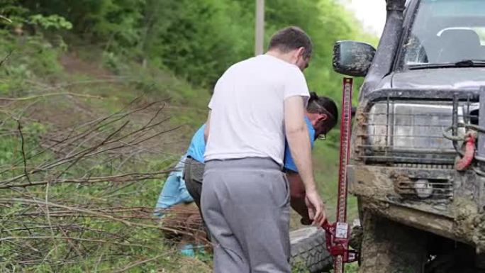 两名旅客在森林肮脏的道路上更换了expeditionaty SUV的车轮。