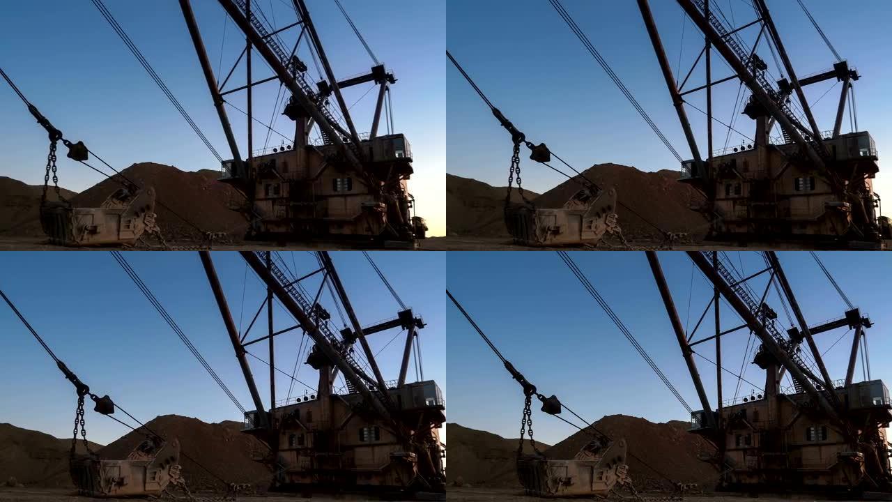 PAN拍摄拖网超重型挖掘机站在采石场边，夕阳映衬下的蓝天。