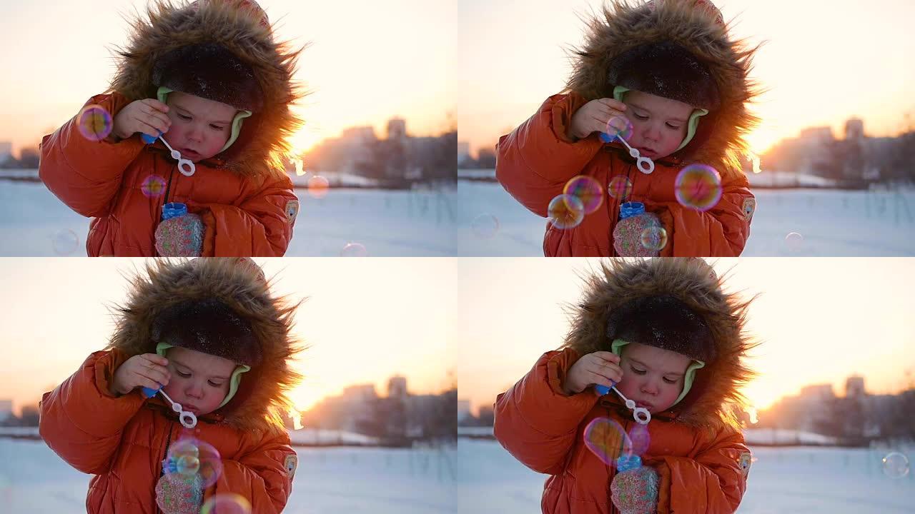 男孩在冬天的日落时在公园里吹肥皂泡