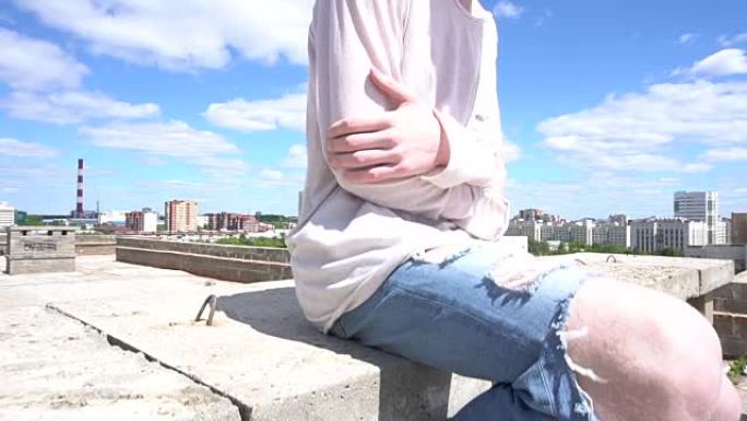 穿着白色运动衫的年轻红发男子坐在屋顶的砖墙上
