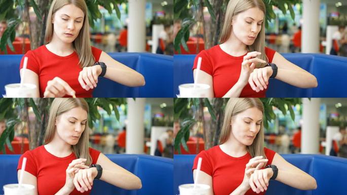 穿着红色t恤的女人坐在咖啡馆里，用她的智能手表，和吃薯条的朋友聊天