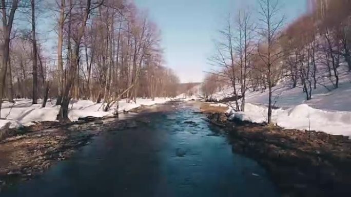 在雪中穿越美丽的春天森林飞过溪流