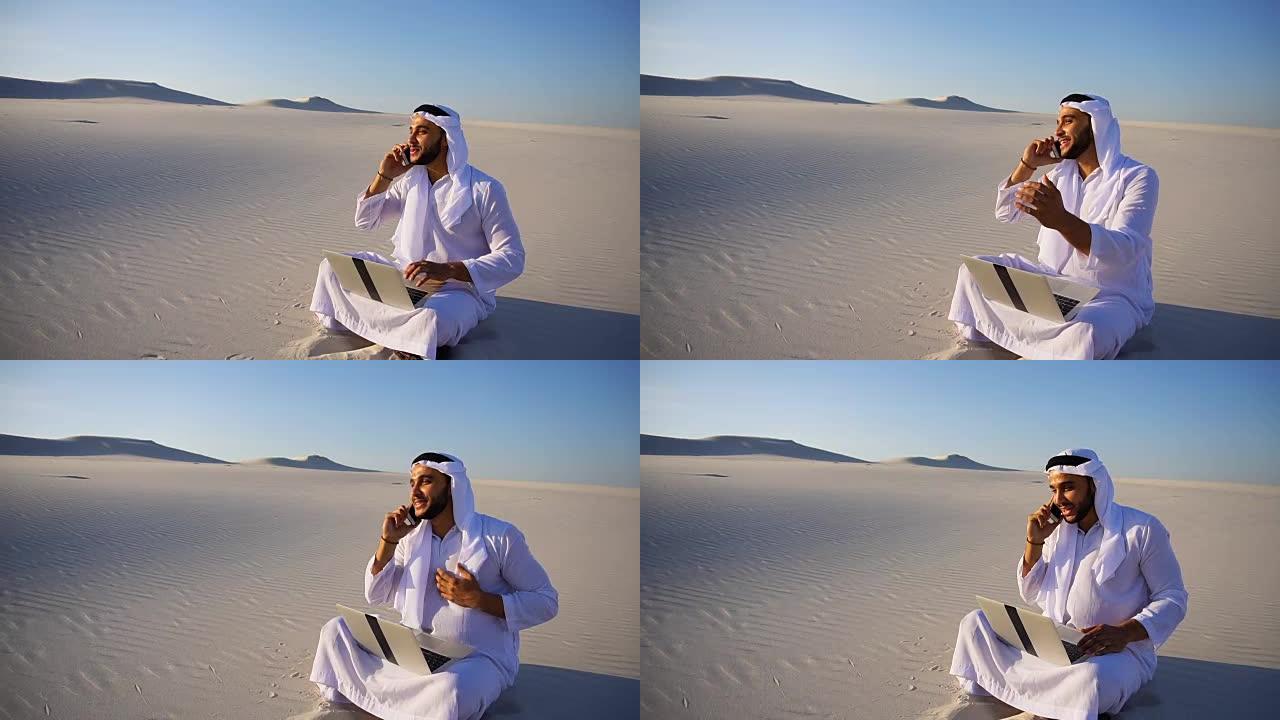 在夏天的大沙漠里，英俊的阿拉伯阿拉伯酋长男商人叫商业伙伴坐在沙地上，带着笔记本电脑