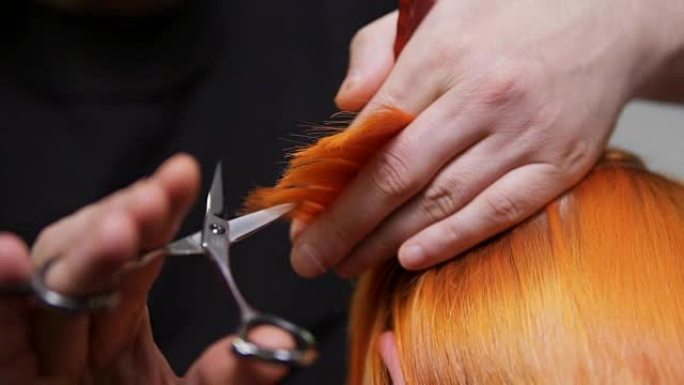 美容院的专业理发师剪头发的特写镜头。男性手握着一根发束，用剪刀和梳子将其剪掉。慢动作镜头