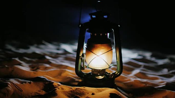 老式油灯站在沙滩上，在黑暗中发光