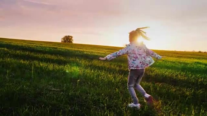 一个无忧无虑的女孩朝着日落的绿色田野奔跑。概念-快乐的童年，轻盈和自由。Steadicam射击