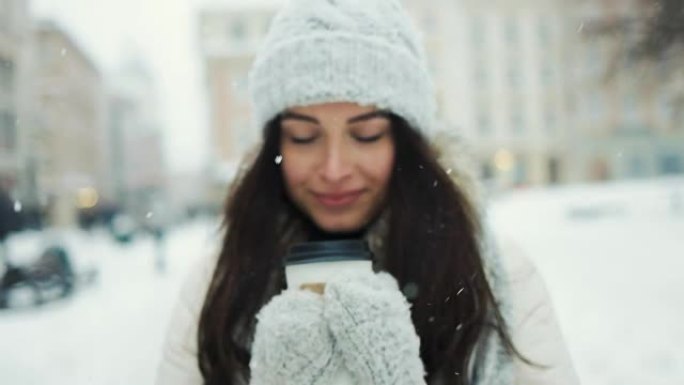 幸福，寒假，圣诞节，饮料和人们的概念-微笑的年轻女子穿着白色暖和的衣服与喝咖啡带走了雪城背景