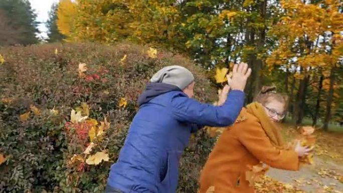 父亲和女儿在秋季公园玩耍。然而，他们微笑着笑。爸爸把树叶扔在一个少年的头上
