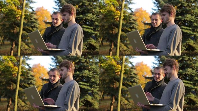 两个微笑的创业商人在秋天在公园户外讨论共享笔记本电脑