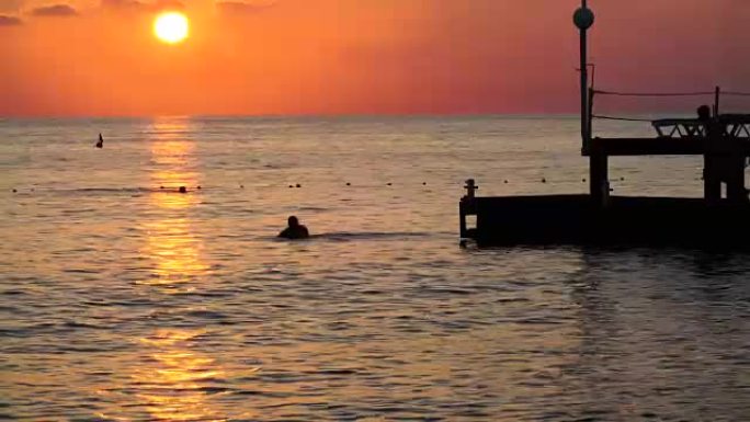 海上美丽的日落。盖伊从码头跳入地中海的剪影