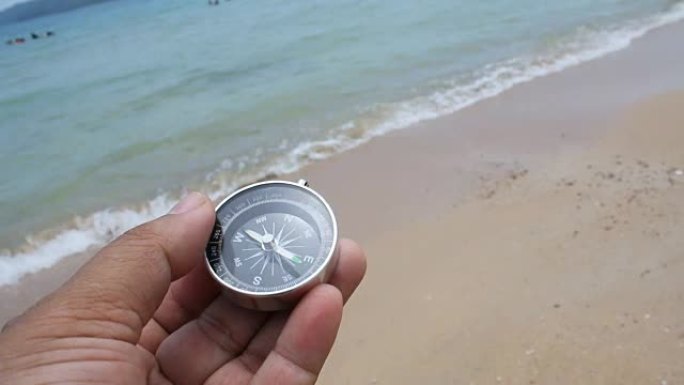 mand的近距离拍摄手在沙滩上拿着指南针，具有自然的海洋和风的环境声音