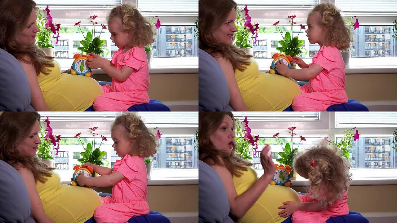 孕妇妈妈女人和可爱的女儿女孩在肚子上玩玩具时钟