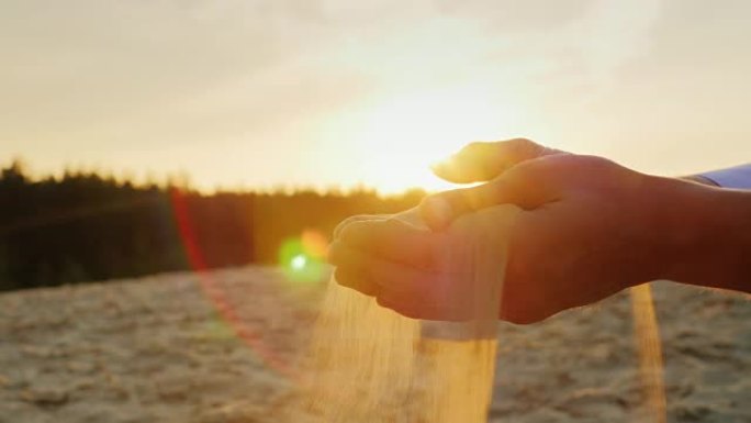 日落时，沙子从男人的手中倾泻出来。概念: 时间的短暂，改变寿命