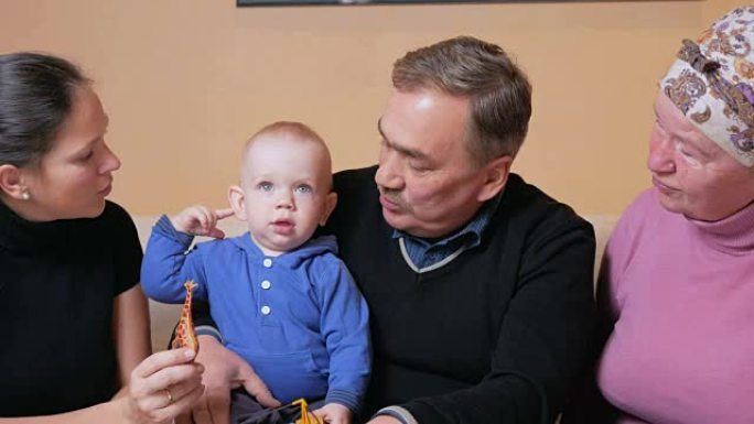 有一个婴儿的幸福大家庭她的母亲和祖父母在沙发上玩得开心。他们彼此欢笑和交谈。家庭幸福的概念