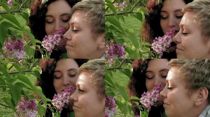 两个女孩在绿色公园里嗅丁香花