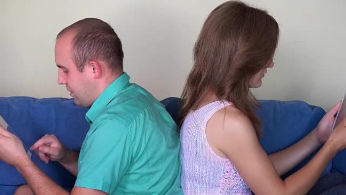 男人和女人使用平板电脑背靠背坐在沙发上。特写