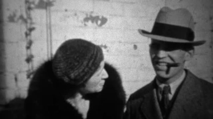 1933: 软呢帽男子在黑色皮大衣中与忠诚的妻子抽雪茄。