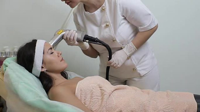 闭着眼睛的女人在美容院接受照片嫩肤程序。美容师为女人完成照片嫩肤美容程序。皮肤护理。年轻女子接受面部
