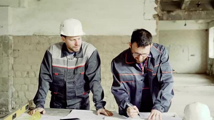 戴着防护头盔的工程师和工头在施工图中做笔记，这些人正在一家工厂里进行侦察