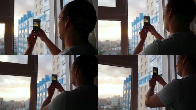 在令人惊叹的日落期间，年轻人用手机用玻璃窗在城市上空慢动作拍照