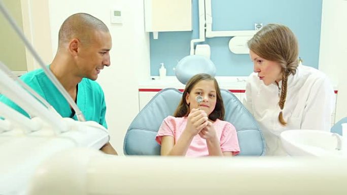 牙科医生和牙医在检查前向小女孩展示口腔镜